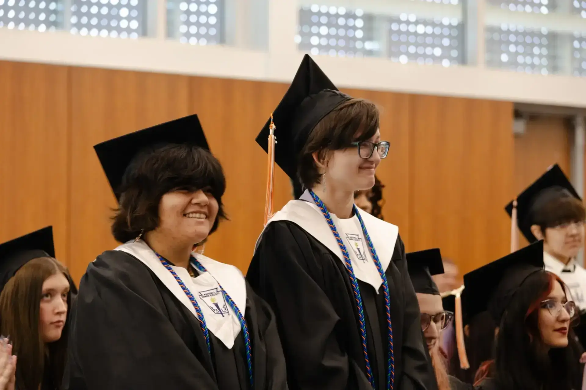 Estudiantes con toga y birrete sonríen durante una ceremonia de graduación.