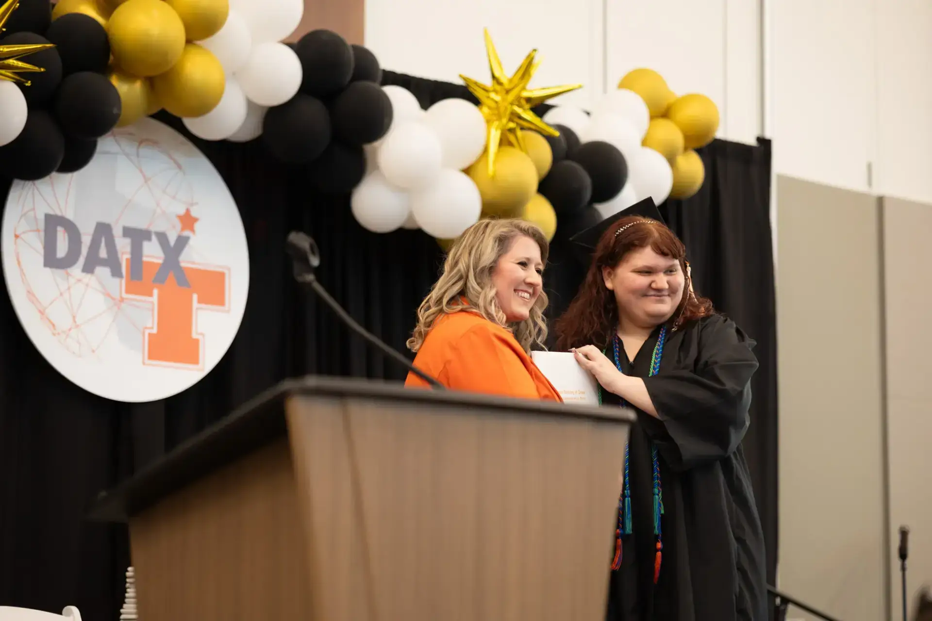 Dos mujeres sonríen durante una ceremonia de graduación.