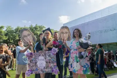 Una alegre escena de graduación al aire libre con un graduado con toga y birrete sosteniendo flores.